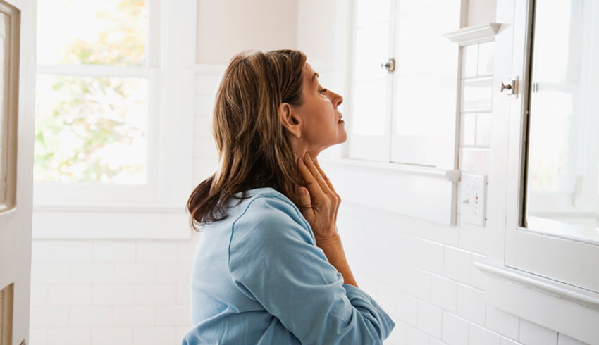 A woman examines her neck as she looks into a mirror